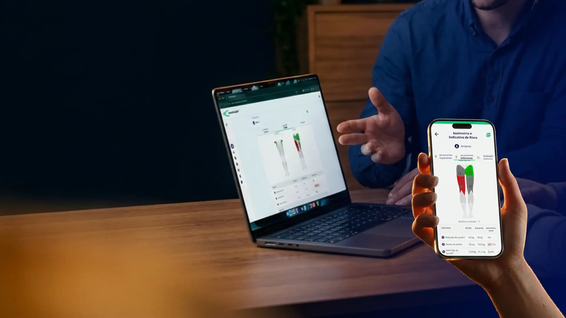 Fisioterapeuta e paciente analisando relatório de assimetria muscular no app Kinology, no laptop e no celular